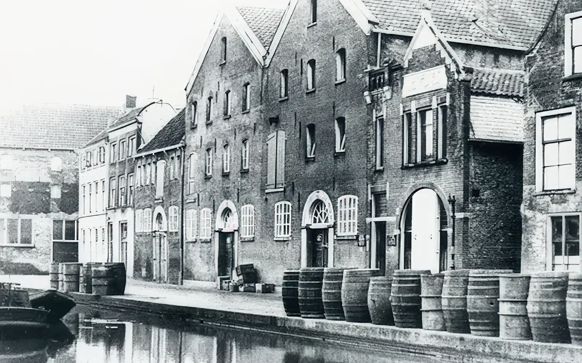 Historische opname van pakhuizen aan het water in Schiedam, met jeneverton­nen op de kade